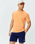 Mens Dash Bunny Sport Tee, a peach jersey t-shirt with a small white embroidered Psycho Bunny logo on the left chest, paired with navy shorts featuring a matching logo and a striped Psycho Bunny baseball cap.
