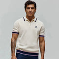 Mens Dax Knit Polo, cream pique knit with classic fit, featuring navy and pink tipped collar, cuffs, and hem, plus a small embroidered navy Psycho Bunny skull logo on the left chest.