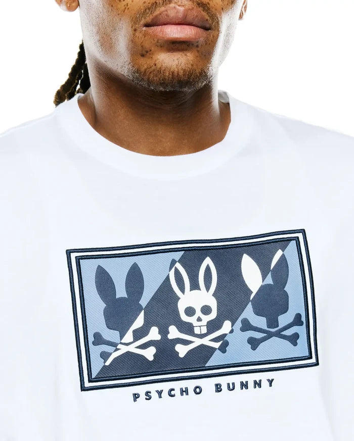 Mens Desmond Graphic Tee in white jersey knit, featuring a large chest graphic with three bunny skull and silhouette designs in white, light blue, and dark blue on a patterned background, bordered in dark blue, with PSYCHO BUNNY text below.