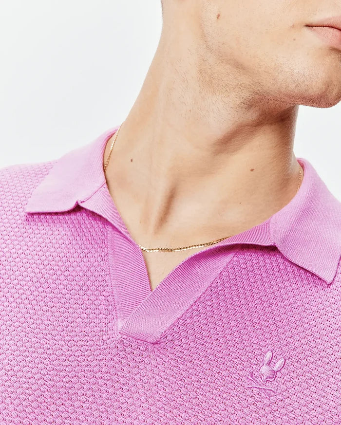 Bright pink Mens Devon Knit Polo with a textured knit body, ribbed V-neck collar, and a small, tone-on-tone embroidered Psycho Bunny skull logo on the left chest.