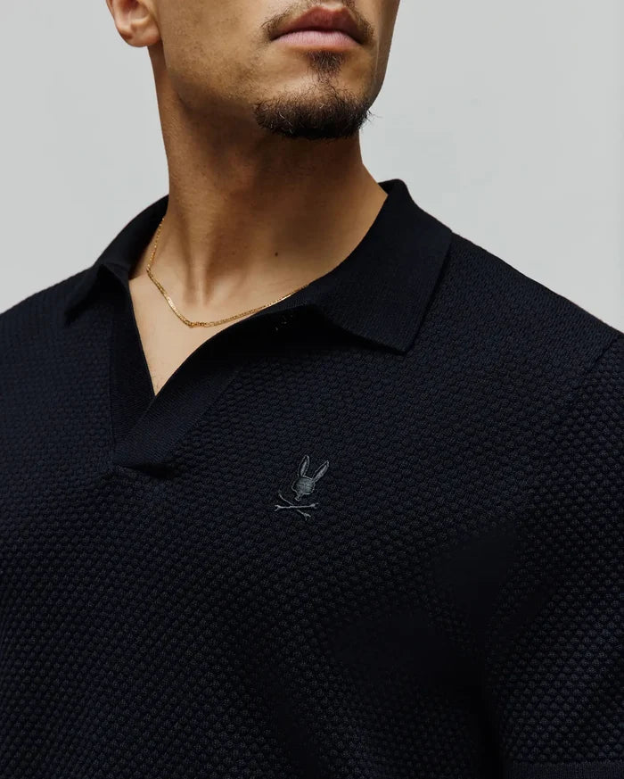 Mens Devon Knit Polo in navy, featuring a textured knit fabric, spread collar, V-neck placket, and a small, tonal embroidered Psycho Bunny skull logo on the left chest.