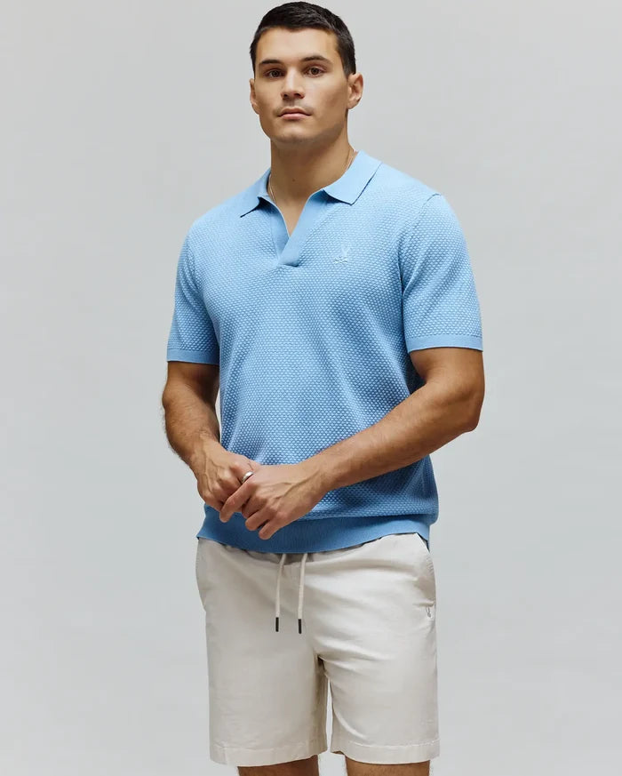 MENS DEVON KNIT POLO in sky blue, a classic fit, short-sleeve polo with a textured knit fabric, open collar, and a small, tonal embroidered Psycho Bunny skull logo on the left chest.