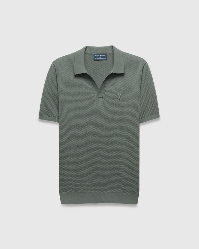 Mens Devon Knit Polo in sage green, a classic fit with textured knit fabric, open collar, and a small tonal embroidered Psycho Bunny skull logo on the left chest.