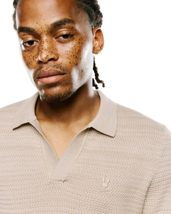 Mens Devon Braided Stitch Knit Polo in beige, featuring a unique braided stitch knit texture, spread collar, V-neck placket, and a small embroidered Psycho Bunny skull logo on the left chest.