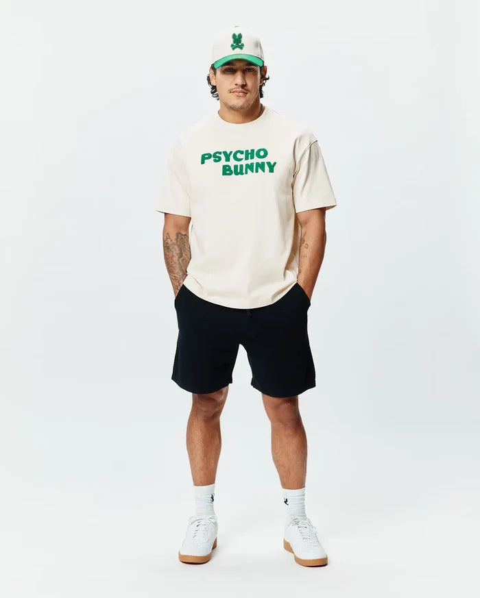 Cream classic fit jersey t-shirt with bold green PSYCHO BUNNY chest text, paired with black Mens Devon Knit Short, a cream and green Psycho Bunny skull logo cap, and white logo socks.
