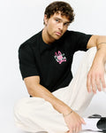 Mens Duncan Relaxed Fit Tee, a black jersey t-shirt with a relaxed fit, featuring a vibrant neon pink and light green Psycho Bunny skull logo graphic print on the chest.