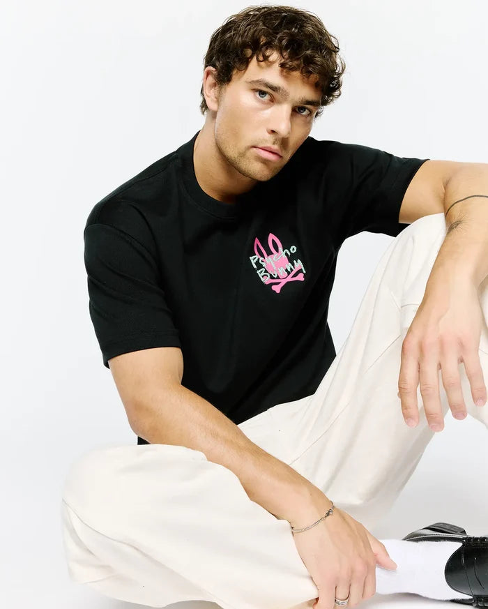 Mens Duncan Relaxed Fit Tee, a black jersey t-shirt with a relaxed fit, featuring a vibrant neon pink and light green Psycho Bunny skull logo graphic print on the chest.