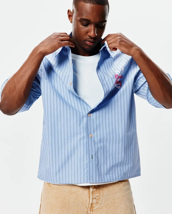 Mens Duncan Stripe Shirt, light blue with vertical white and dark blue stripes, featuring a large embroidered pink Psycho Bunny skull logo and script on the left chest, relaxed fit.