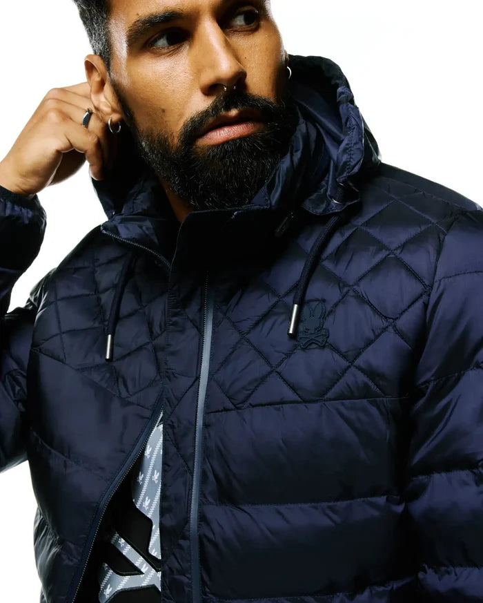Mens Emerik Hooded Puffer Jacket in navy, featuring a diamond quilted upper, full grey zip, and a small embroidered Psycho Bunny skull logo on the left chest. Shiny puffer fabric, classic fit.