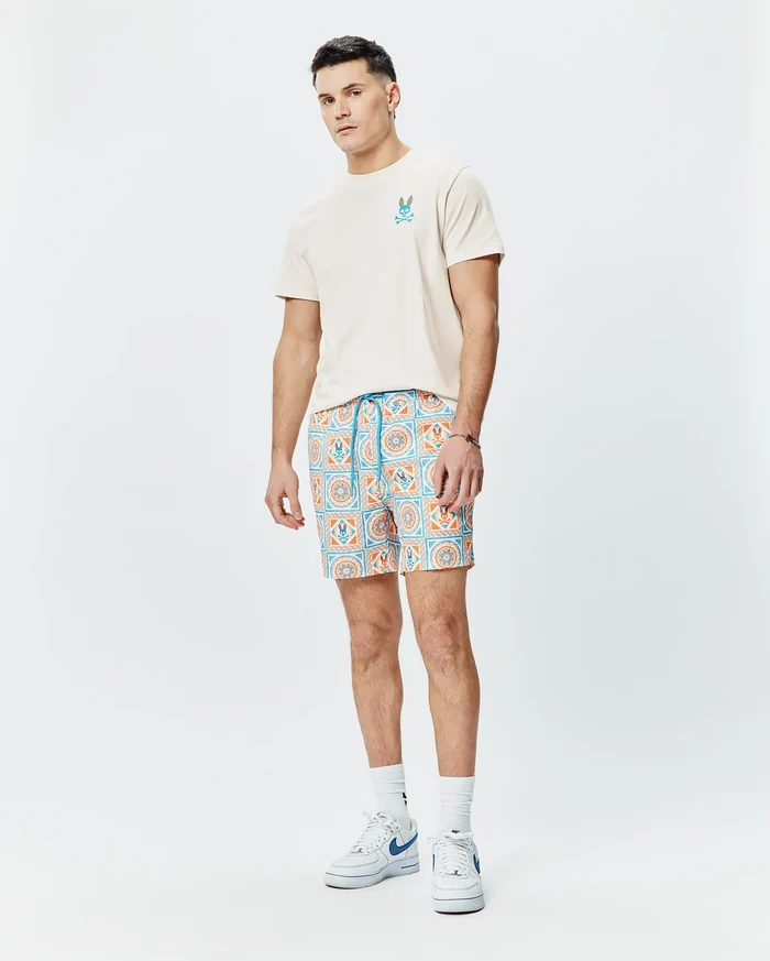 Mens Frank Back Graphic Tee, classic fit beige jersey with embroidered blue/orange Psycho Bunny skull chest logo. Relaxed shorts, all-over blue/orange geometric tile pattern, integrated bunny skull logos, blue drawstring.