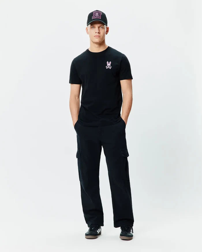 Black Mens Frank Back Graphic Tee, classic fit, with a small pink embroidered Psycho Bunny skull logo on the left chest, complemented by black relaxed cargo pants and a black baseball cap featuring a vibrant pink patterned front.