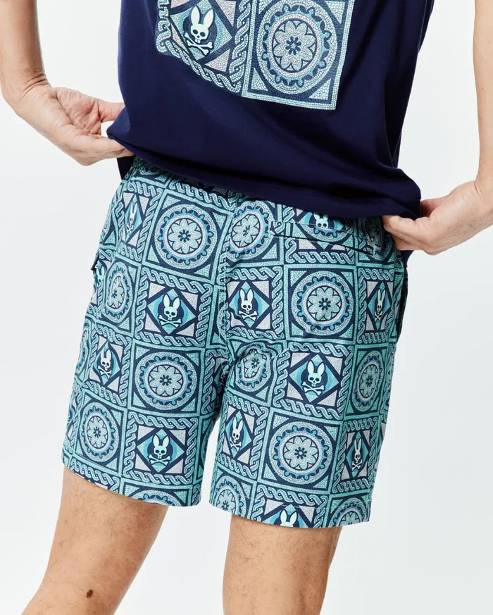 Mens Frank Swim Trunk 6, featuring an all-over mosaic pattern on smooth fabric in teal, light blue, and dark blue, with repeated Psycho Bunny skull logos and floral motifs, in a relaxed fit.