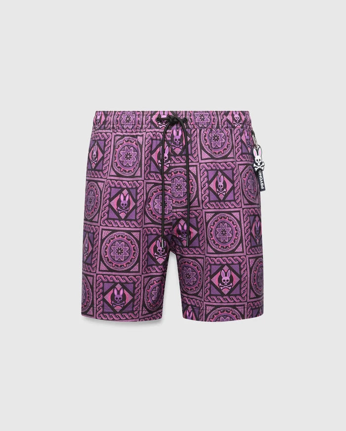 Mens Frank Swim Trunk 6, purple and pink mosaic tile swim trunks with black accents, featuring repeated Psycho Bunny skull logos and floral patterns, classic fit, smooth fabric, and a small rubber Psycho Bunny charm on the drawstring.