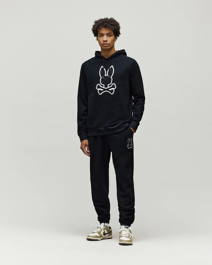 Mens Gage Patch Hoodie: Black relaxed fit French terry hoodie with a large white outlined Psycho Bunny skull logo on the chest, kangaroo pocket, and ribbed cuffs, paired with matching black sweatpants.