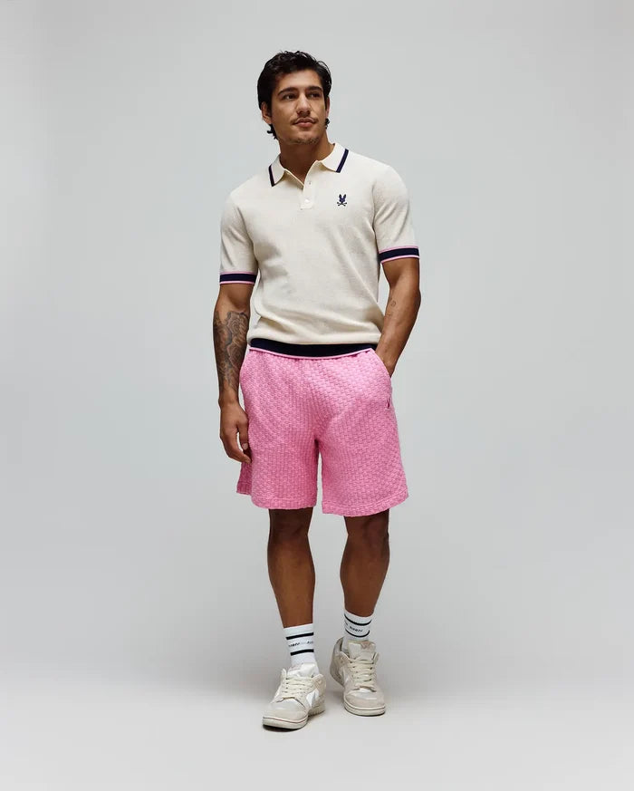 Cream knit polo with navy and pink striped collar/cuffs and embroidered Psycho Bunny logo, paired with bright pink textured knit Mens Garen Knit Short featuring a navy waistband and small bunny skull logo.