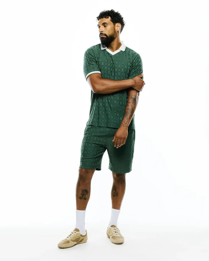 Dark green Mens Garry Jacquard Johnny Collar Polo and matching shorts, featuring an all-over Psycho Bunny skull logo jacquard pattern, classic fit, and white collar with sleeve trim.
