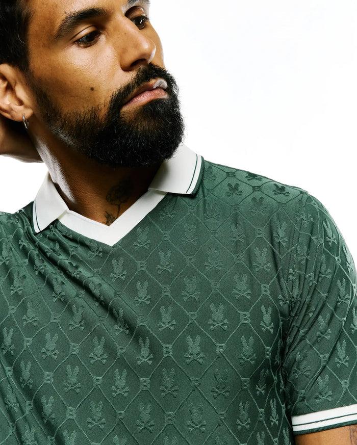 Mens Garry Jacquard Johnny Collar Polo in deep green, featuring an all-over textured Psycho Bunny skull logo pattern, with a white Johnny collar and ribbed cuffs accented by green stripes.