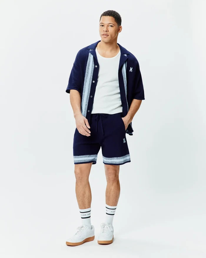 Mens Giles Knit Short 7, a relaxed fit navy knit short with light blue striped hem and embroidered Psycho Bunny logo. Complemented by a matching navy knit shirt with striped placket.