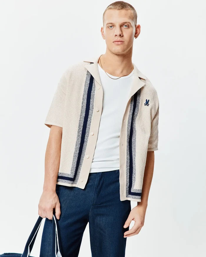 Mens Giles Relaxed Fit Border Knit Shirt in beige textured knit, featuring navy and light blue vertical stripes, a camp collar, and a small embroidered navy Psycho Bunny skull logo on the left chest.