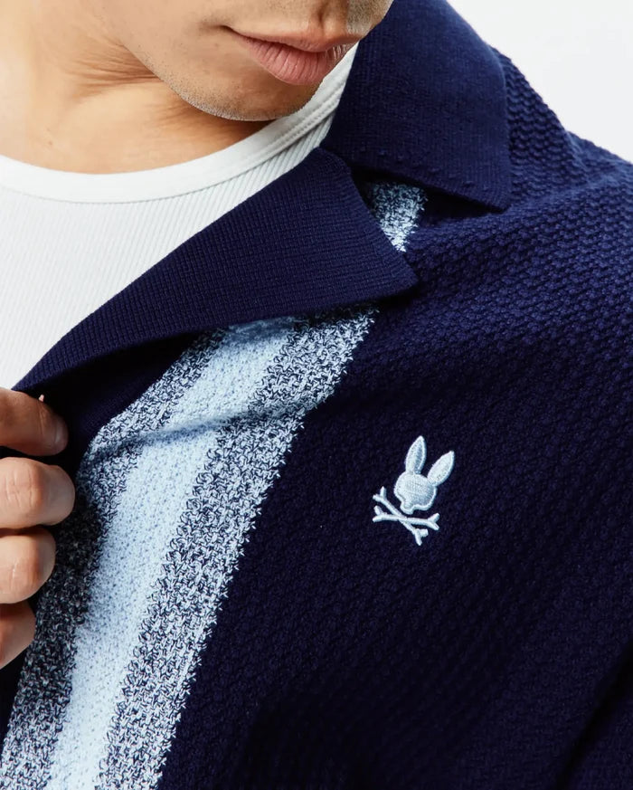 Mens Giles Relaxed Fit Border Knit Shirt in navy blue with light blue and white textured stripes, featuring a classic collar and a small embroidered Psycho Bunny skull logo on the chest.