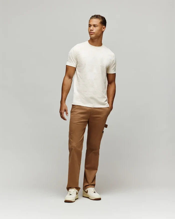 Mens Gio Tee cream textured jersey t-shirt with an all-over embossed checkerboard pattern featuring the iconic Psycho Bunny skull logo, designed for a comfortable classic fit.