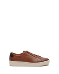 The Vince Camuto Men’s Hallman Casual Sneaker showcases a stylish brown leather design with tan laces, a white rubber sole, and a dark brown heel patch. Presented in side profile against a plain white background, these sneakers blend everyday comfort with modern style.