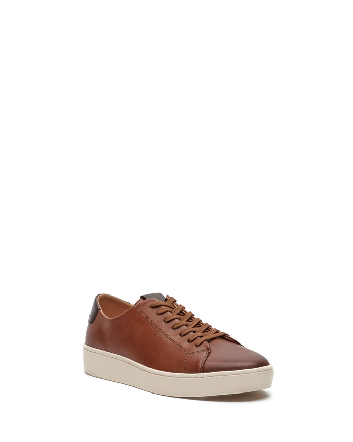 Introducing the Men’s Hallman Casual Sneaker from Vince Camuto—a stylish brown leather sneaker featuring tan laces, a crisp white rubber sole, and a sleek black heel accent. Displayed on a white background, this shoe is perfect for anyone seeking both comfort and style.