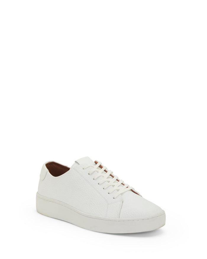The Vince Camuto Men’s Hallman Casual Sneaker—a stylish white low-top with a textured surface, crisp white laces, and a flat sole—demonstrates modern fashion footwear as it’s showcased at an angle against a simple white background.