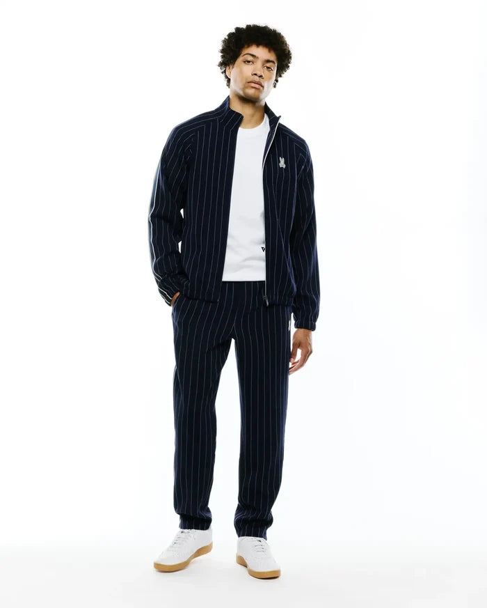 Mens Harland Double Weave Chalk Stripe Track Pant and matching full-zip jacket. Navy blue relaxed fit tracksuit with white pinstripes, green sleeve stripe, and embroidered Psycho Bunny skull logo.