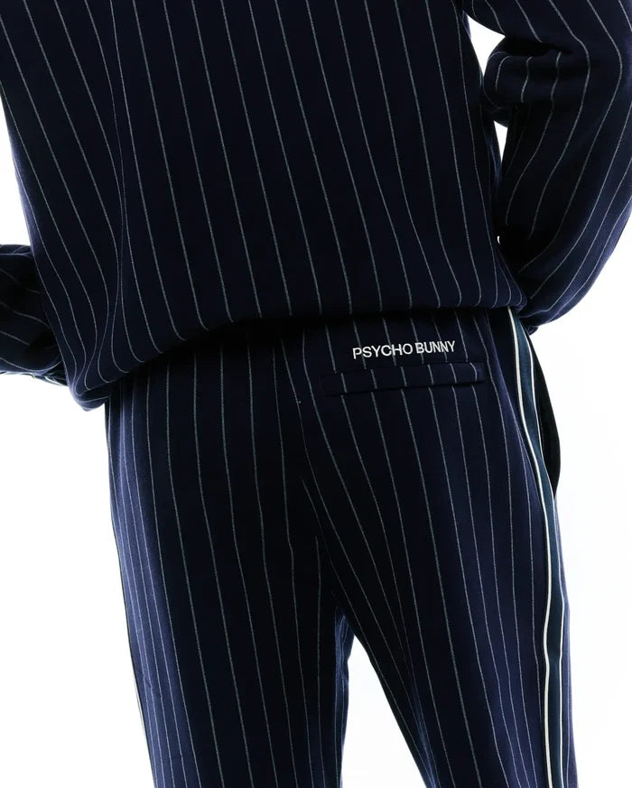 Mens Harland Double Weave Chalk Stripe Track Pant, navy with fine white pinstripes, a relaxed fit, and a prominent white side stripe. White embroidered PSYCHO BUNNY branding is on the back flap pocket.