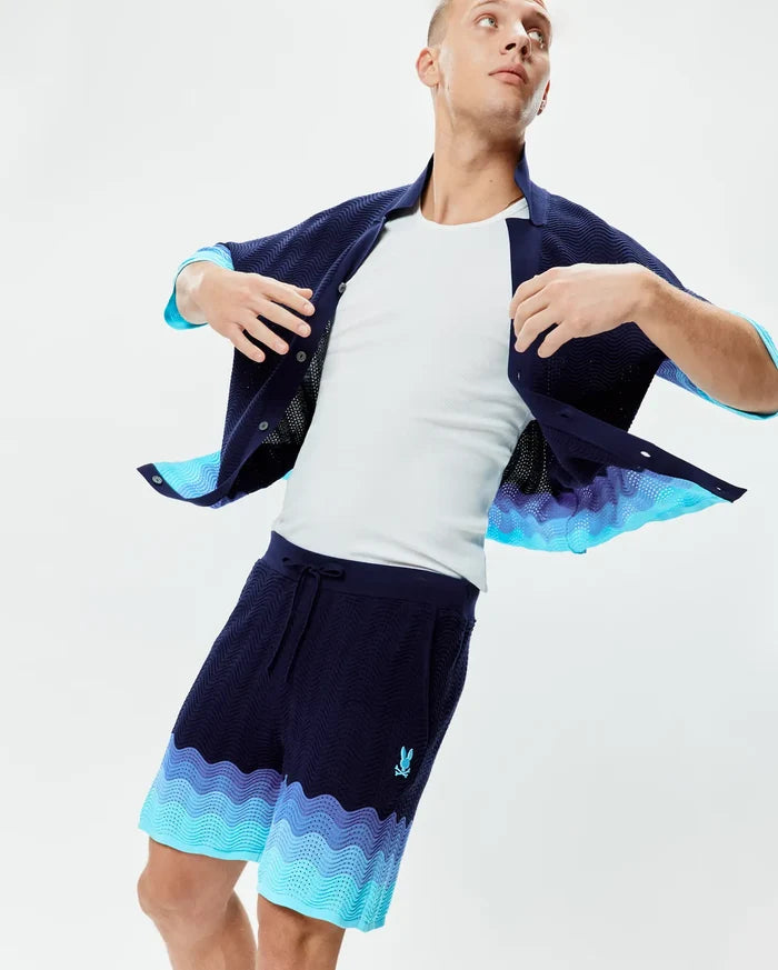 Mens Holden Knit Short 6 in navy, featuring a wavy knit texture, relaxed fit, gradient light blue and purple wave pattern at the hem, and an embroidered Psycho Bunny skull logo on the left thigh.