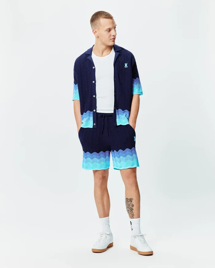 Navy blue knit short-sleeve shirt and Mens Holden Knit Short 6, featuring a wavy light blue to turquoise gradient pattern. Small embroidered Psycho Bunny skull logo on left chest and right thigh, in a relaxed fit.