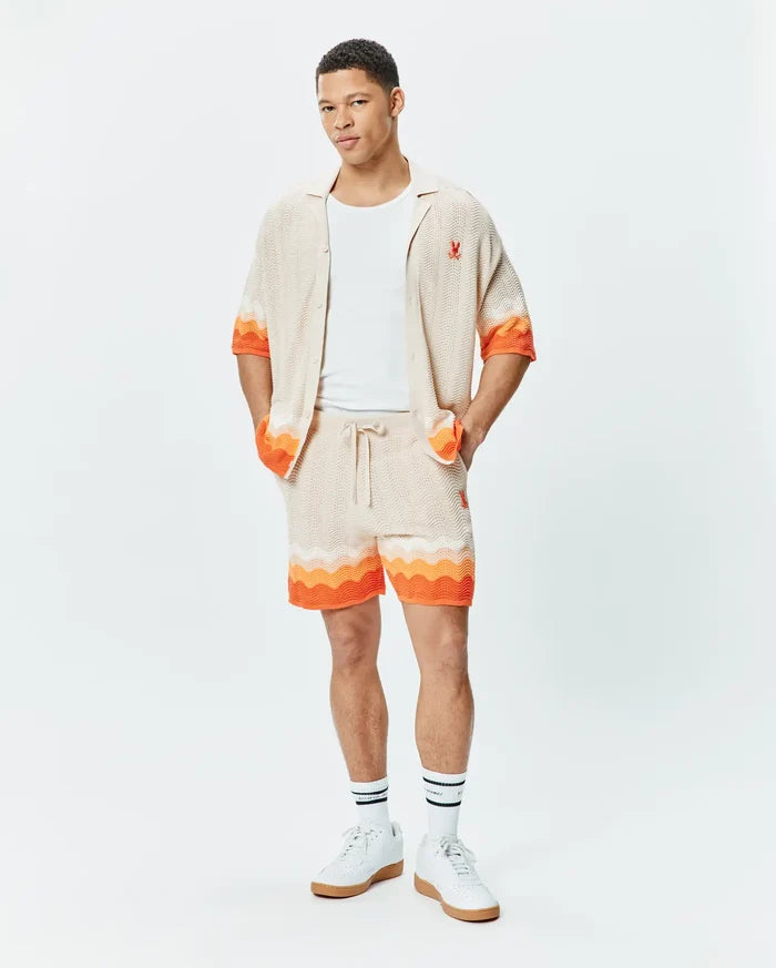 Beige knit short-sleeve shirt and matching Mens Holden Knit Short 6, both featuring a wavy knit texture with vibrant orange accents and a small embroidered orange Psycho Bunny skull logo on the shirt's chest.
