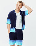 Mens Holden Oversized Knit Shirt in navy blue, an oversized wavy knit with light blue to turquoise color-blocked wave patterns on the hem and sleeves, featuring a small embroidered Psycho Bunny skull logo on the left chest.