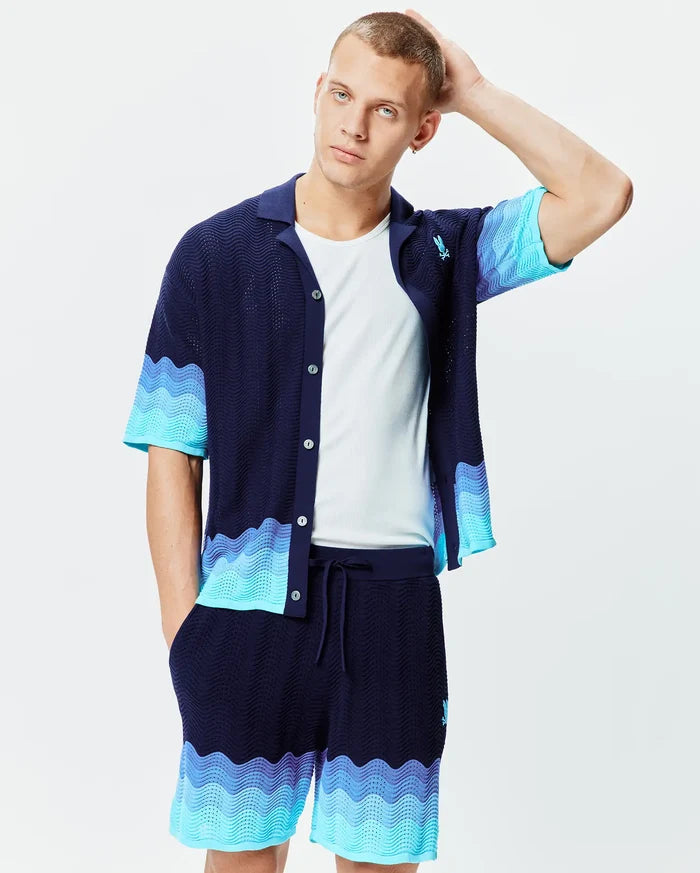 Mens Holden Oversized Knit Shirt in navy blue, an oversized wavy knit with light blue to turquoise color-blocked wave patterns on the hem and sleeves, featuring a small embroidered Psycho Bunny skull logo on the left chest.