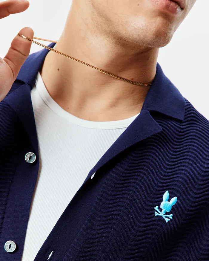 Mens Holden Oversized Knit Shirt in navy blue, featuring a distinct wavy knit texture, a small light blue embroidered Psycho Bunny skull logo on the left chest, and branded silver buttons.