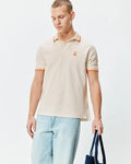 Mens Holden Pique Polo in classic fit, light beige pique with orange tipped collar and cuffs, featuring a small embroidered orange Psycho Bunny skull logo on the left chest.