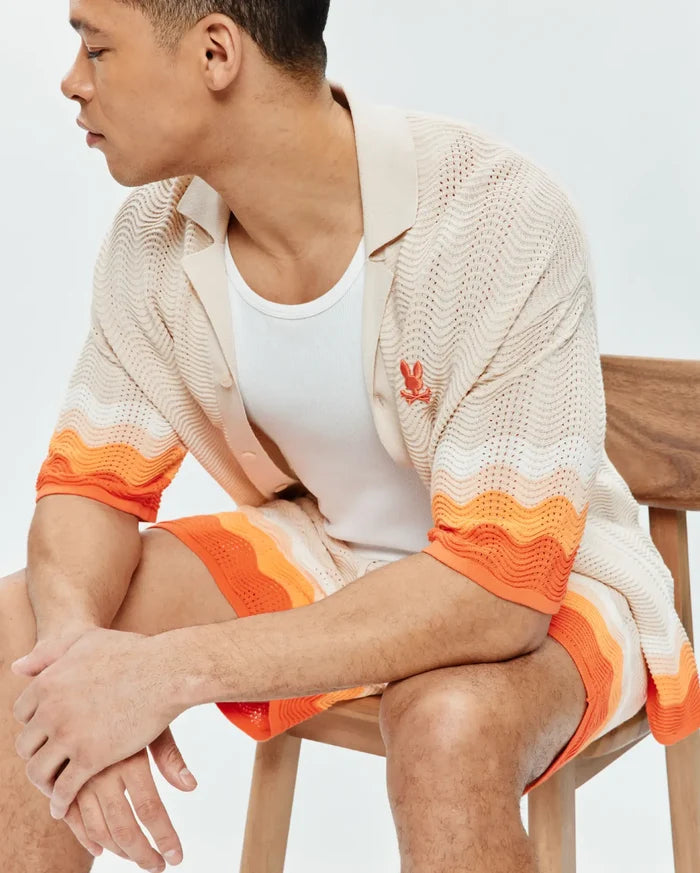 Mens Holden Relaxed Fit Knit Shirt, a beige open-knit with wavy texture, orange and white color block stripes on sleeves, and a small embroidered orange Psycho Bunny logo on the chest, paired with matching knit shorts.