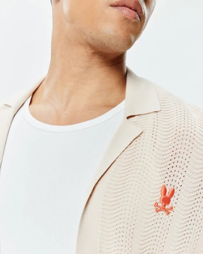 Mens Holden Relaxed Fit Knit Shirt in ecru, featuring an open-knit wavy pattern, a classic collar, and a small embroidered orange Psycho Bunny skull logo on the left chest.