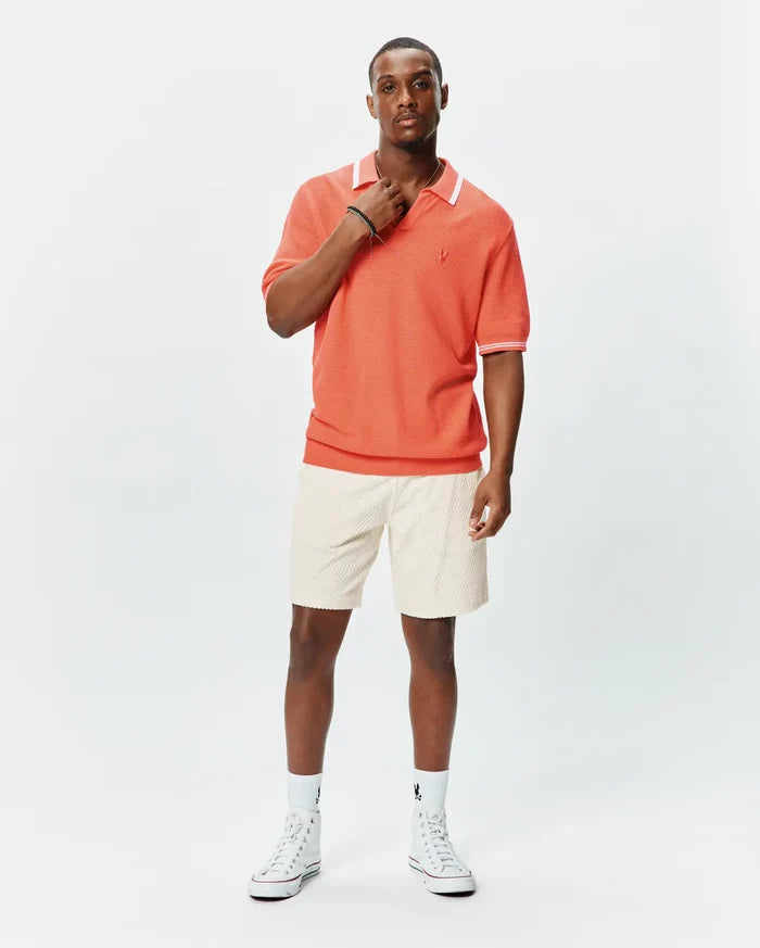 Mens Innis Polo in vibrant coral pique knit, featuring a classic fit, white collar with thin stripe, white sleeve cuffs with thin stripe, and a small embroidered Psycho Bunny skull logo on the left chest.