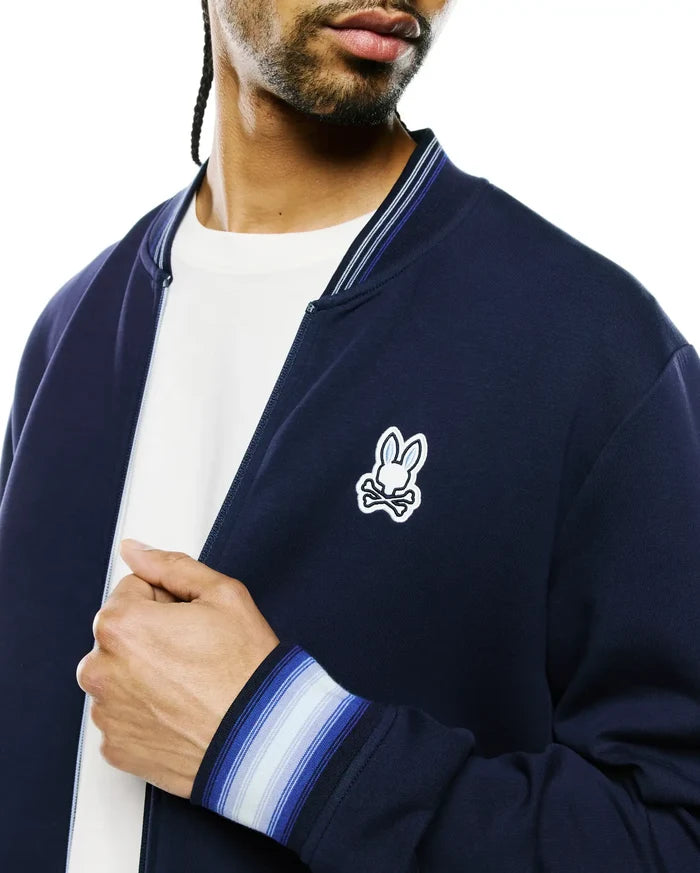 Mens Jaydon Track Jacket, navy smooth knit, classic fit, with a full zip, striped ribbed collar and cuffs in white and blue, and an embroidered white and light blue Psycho Bunny skull logo on the left chest.