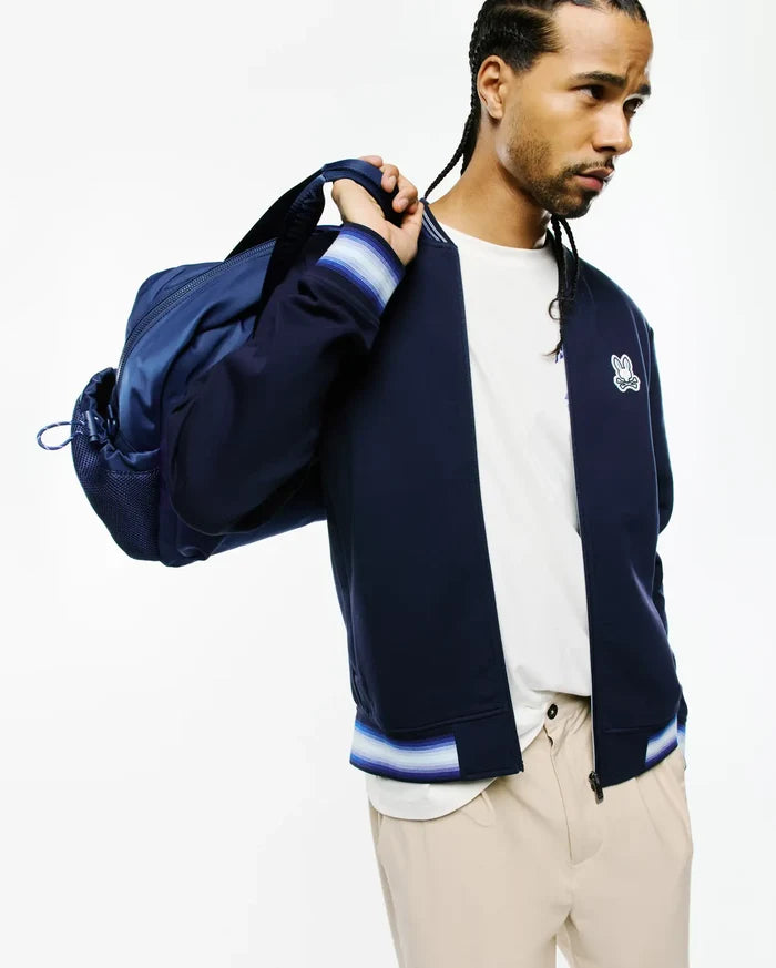 Mens Jaydon Track Jacket in navy blue, a classic fit with smooth fabric, full zip, and ribbed cuffs and hem featuring white, light blue, and purple stripes. Embroidered Psycho Bunny skull logo on the left chest.