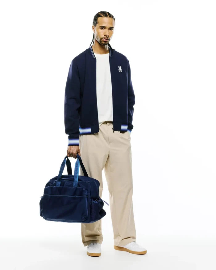 Mens Jaydon Track Jacket, navy blue with white and blue striped ribbed collar, cuffs, and hem. Features a small embroidered white Psycho Bunny skull logo on the left chest. Classic fit, smooth knit fabric.