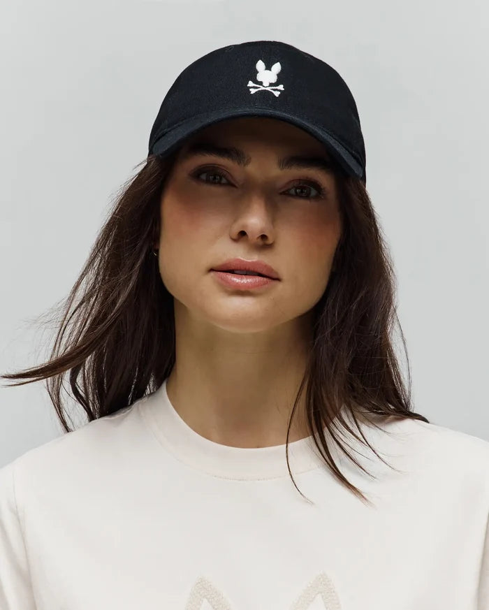 Black cotton twill Jimmy Baseball Cap with prominent white embroidered Psycho Bunny skull logo, paired with a classic fit off-white jersey t-shirt featuring a large textured chest graphic.