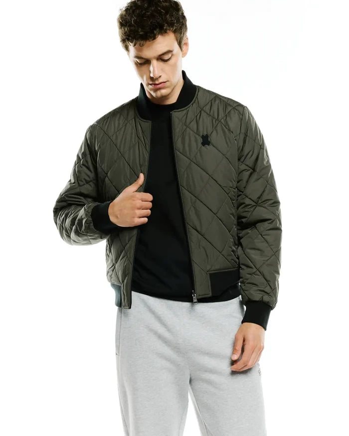 Mens Joaquin Mix Media Reversible Bomber in olive green with diamond quilting, black ribbed collar, cuffs, and hem, featuring a small black embroidered Psycho Bunny skull logo on the left chest.