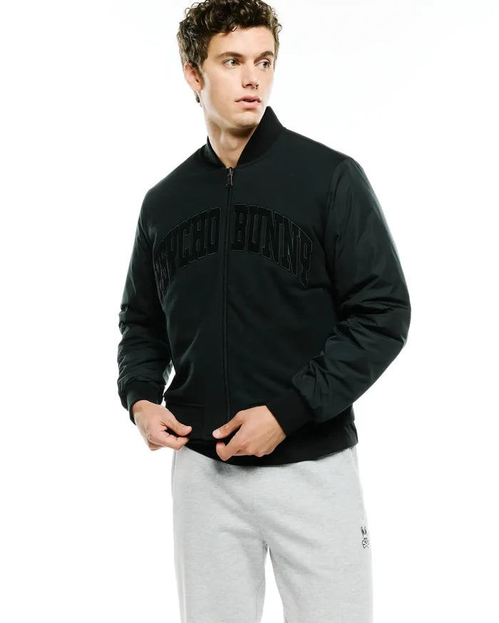 Mens Joaquin Mix Media Reversible Bomber in dark green, featuring a classic fit, full zip, ribbed black collar, cuffs, and hem, with a large arched black PSYCHO BUNNY text logo across the chest and contrasting sleeve fabric.