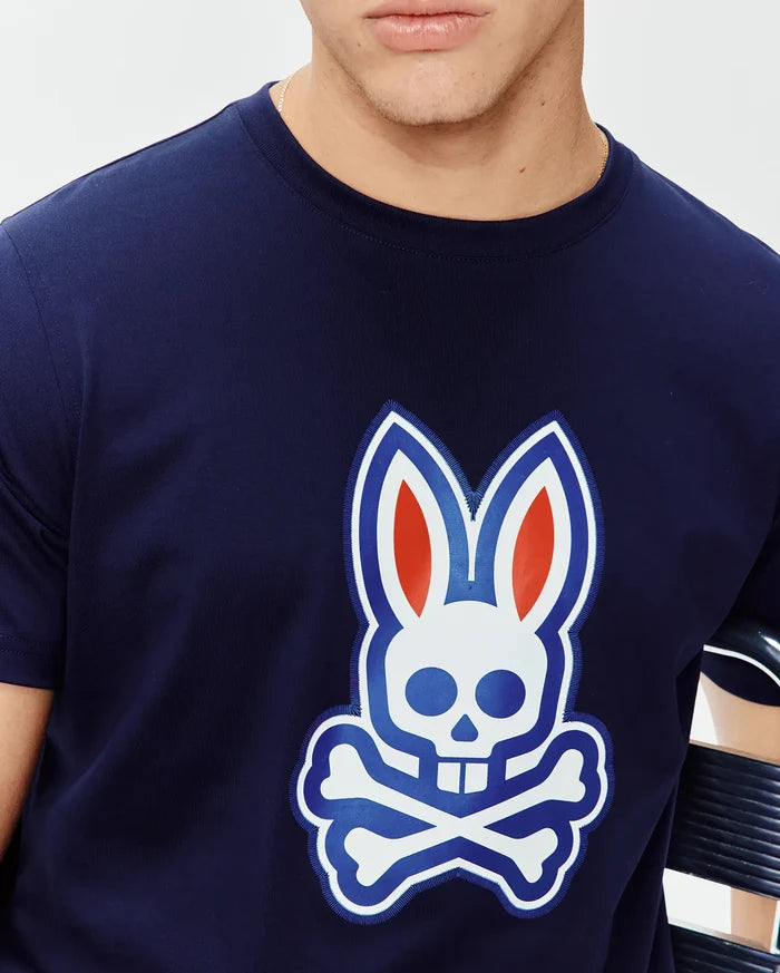 Mens John Graphic Tee, a navy blue classic fit jersey knit t-shirt featuring a large central chest graphic of the iconic Psycho Bunny skull logo in white, blue, and red with an embroidered outline.
