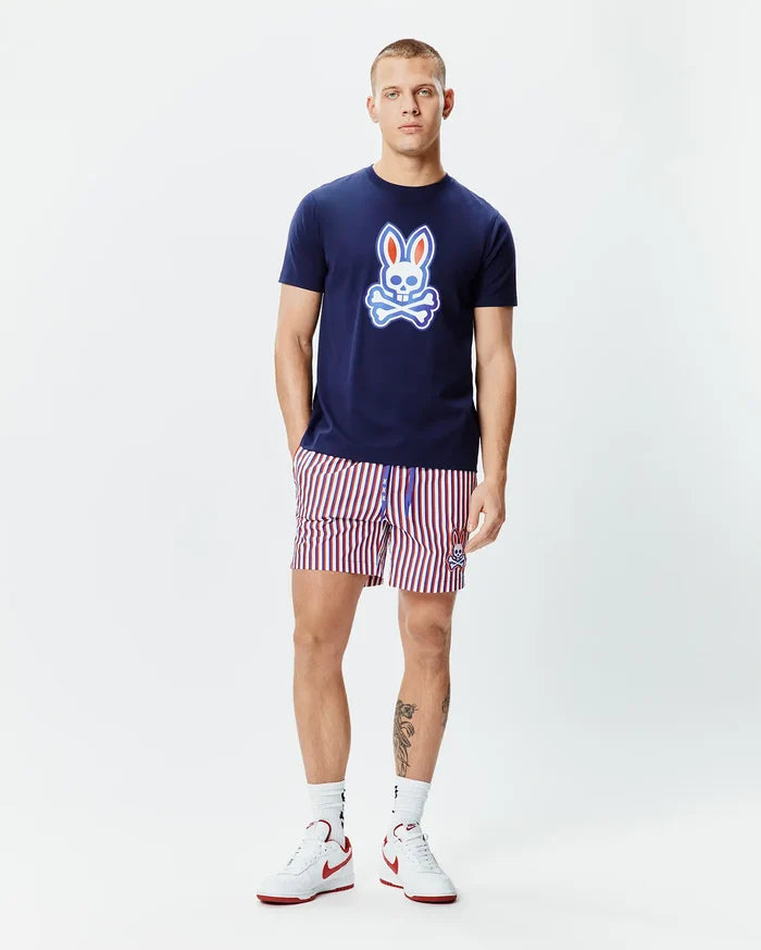 Mens John Graphic Tee, a navy blue jersey t-shirt with a large red, white, and light blue Psycho Bunny skull logo on the chest, paired with red, white, and navy striped shorts featuring a small embroidered bunny logo.