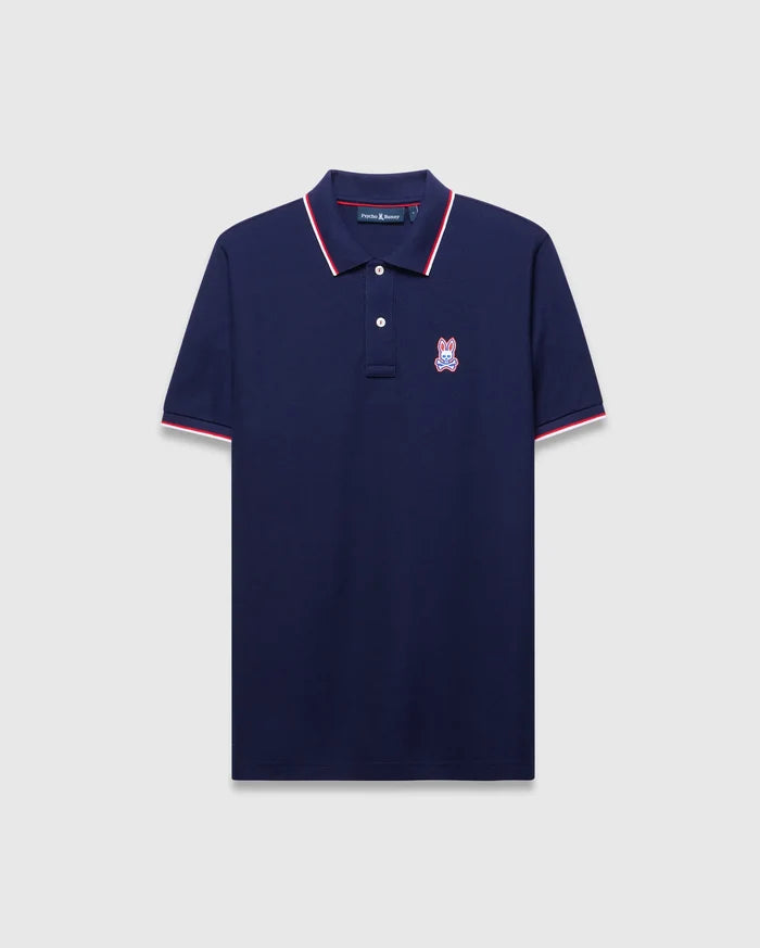 Mens John Pique Polo, a classic fit navy pique polo with red and white tipped ribbed collar and cuffs, featuring an embroidered red, white, and blue Psycho Bunny skull logo on the left chest.