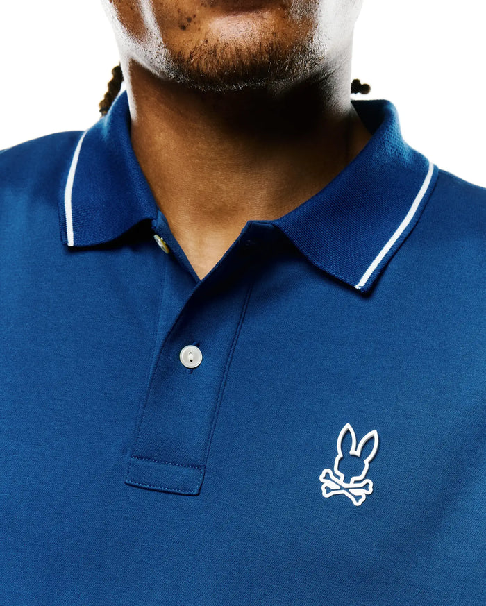 Men's Joji Performance Polo in deep blue performance pique, featuring a ribbed collar with white tipping, two-button placket, and an embroidered white Psycho Bunny skull logo on the left chest.